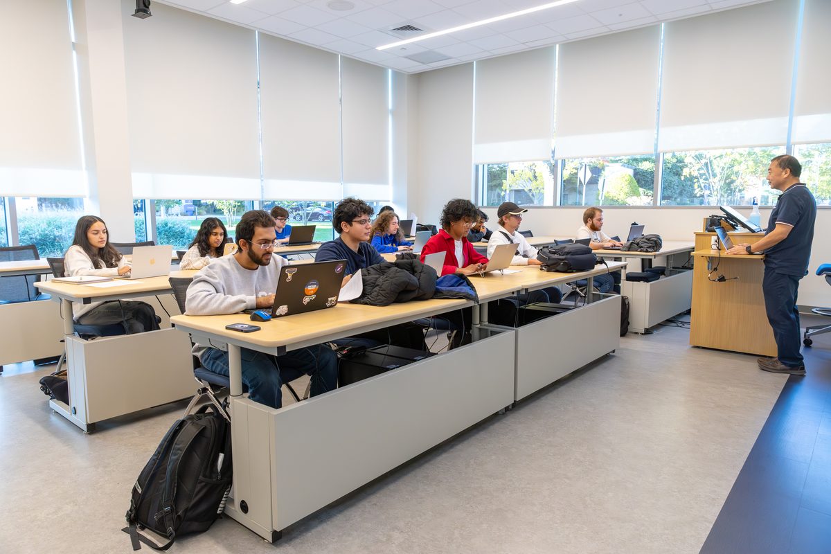 Students at their desks in the Big Data Lab as an instructor teaches from the front, with tall windows along the wall