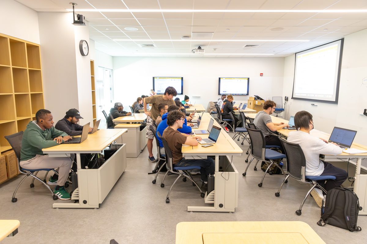 Students working at rows of desks in the Linux Lab, with wall displays and a projection screen at the front